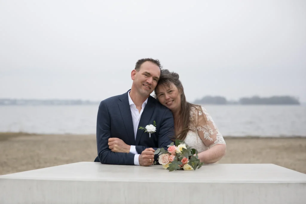 Bruid en bruidegom poseren samen aan het strand tijdens hun bruidsreportage in Ermelo, Nederland