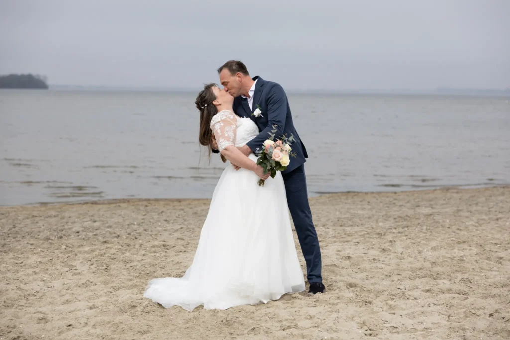Kus tussen bruid en bruidegom op het strand tijdens hun bruidsreportage