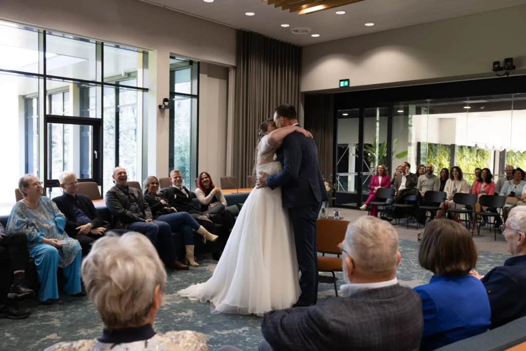Overzichtsfoto van de trouw ceremonie op het gemeente huis. Koppel omhelst elkaar omringd door familie en vrienden.