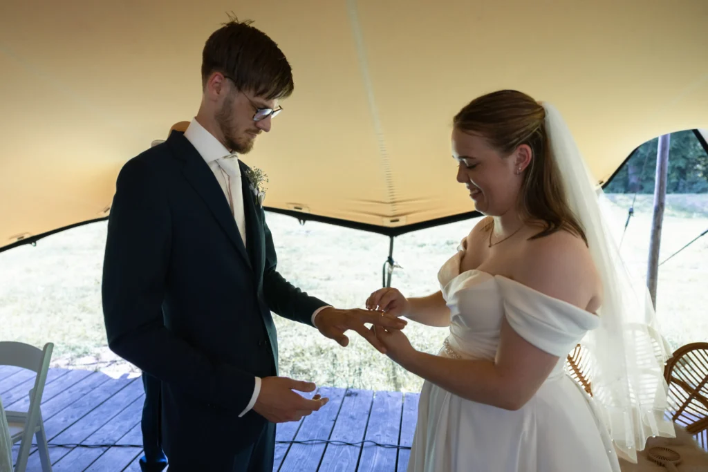 Bruid schuift de trouwring om de vinger van de bruidegom tijdens de ceremonie van hun zomer bruiloft bij de smaeckkamer in Beverwijk
